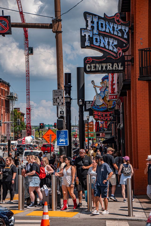 Crowds crossing Broadway in daylight beneath the neon Honky Tonk Central sign in Nashville